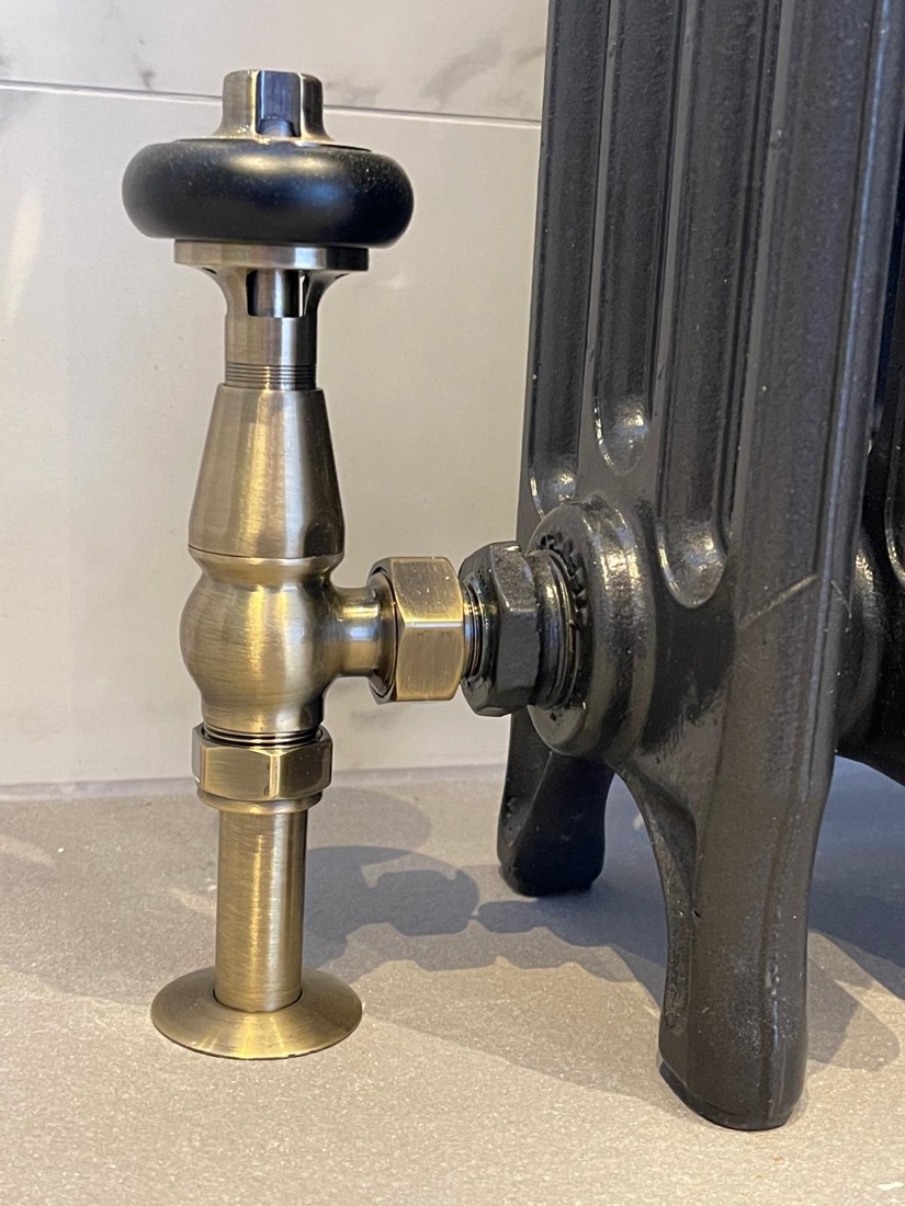 An antique brass radiator valve connected to a cast iron column radiator, finished with clean pipework