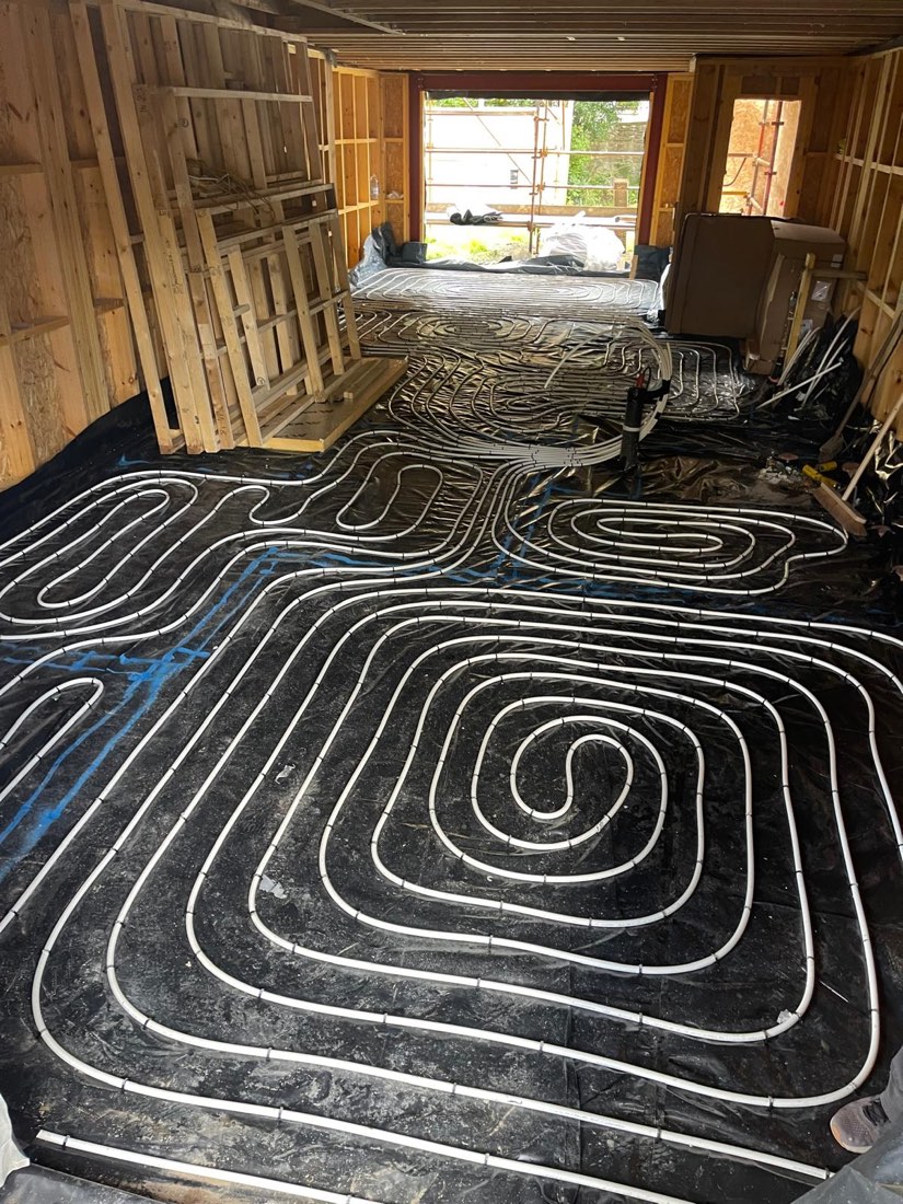 Underfloor heating pipe laid in coils across the floor of a timber-framed extension, clipped down and ready for screed