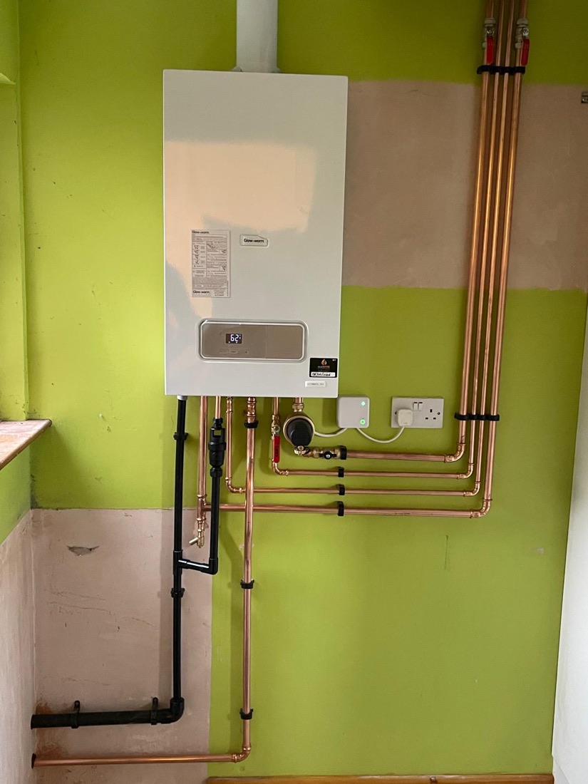 A Glow-worm boiler installed on a green painted wall with copper pipework run along and down