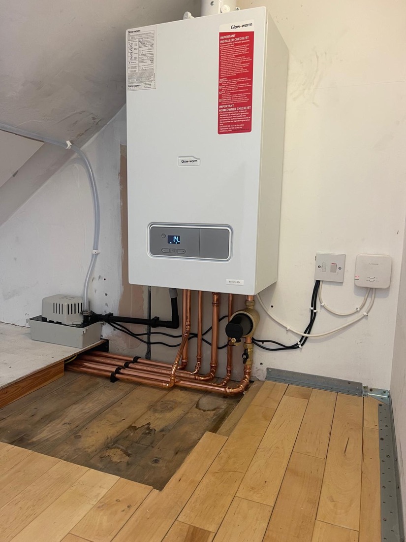 A Glow-worm boiler installed in a loft with copper pipework and a condensate pump