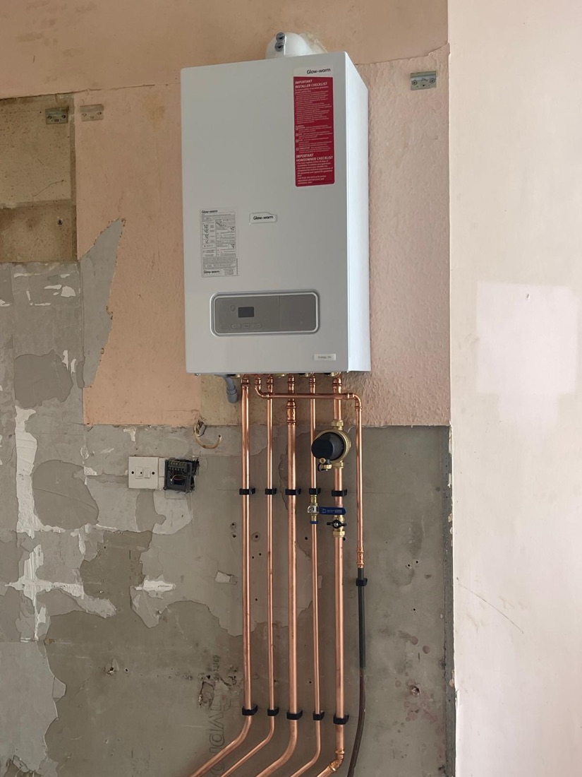 A Glow-worm boiler installed on a part-plastered wall, pipework dropped neatly to the floor