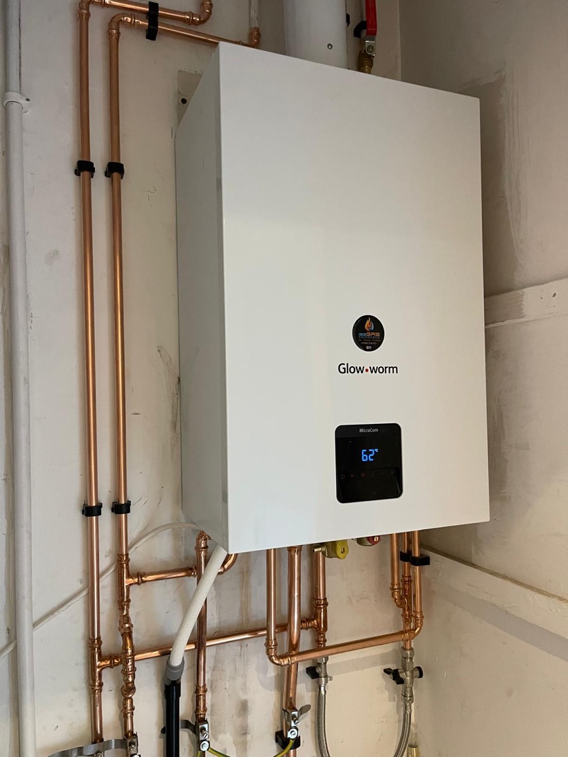 A Glow-worm combi boiler installed with copper pipework run down the wall beside it