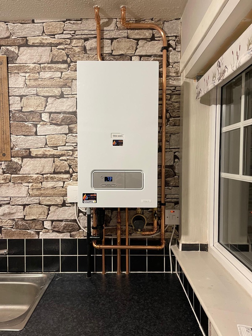A Glow-worm boiler installed against an exposed stone wall with copper pipework