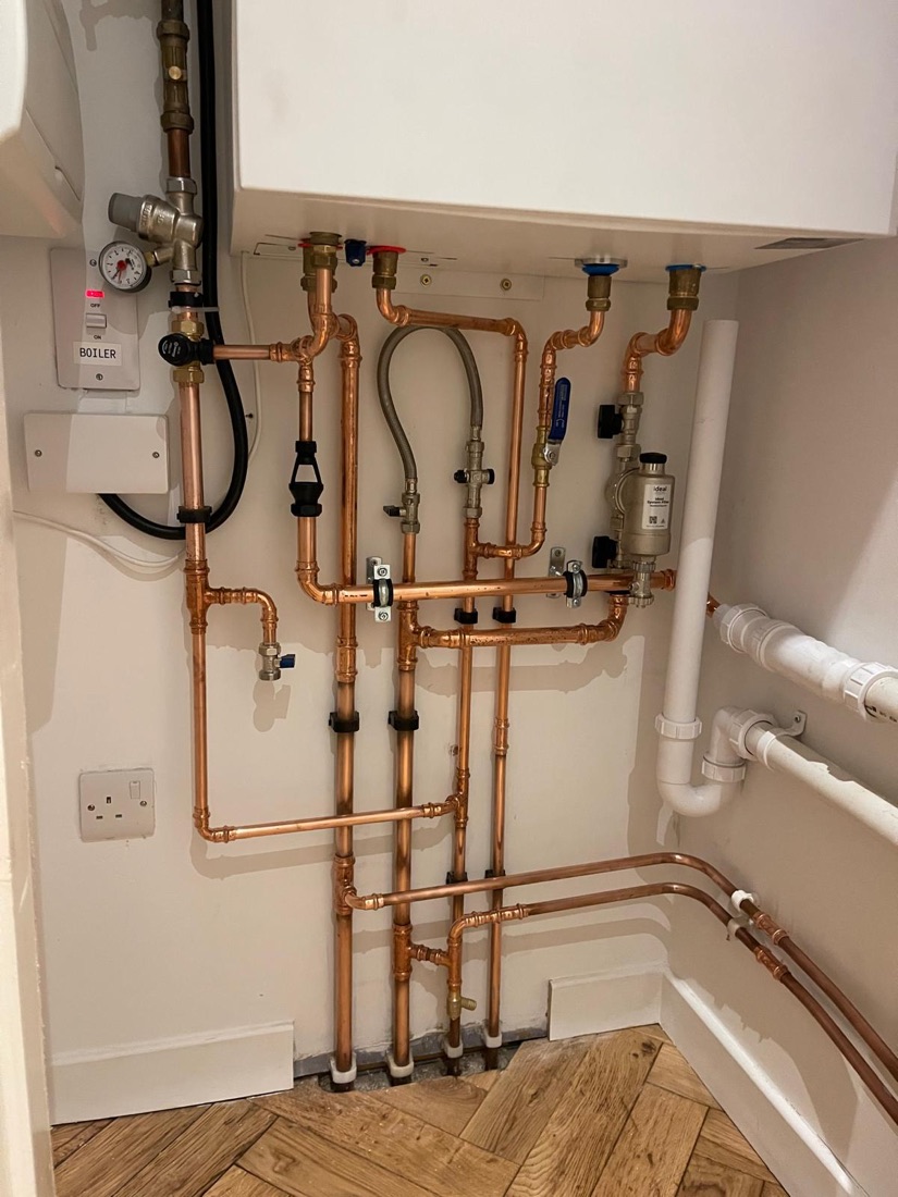 Copper pipework and valves run in a neat parallel bank across a wall behind a boiler
