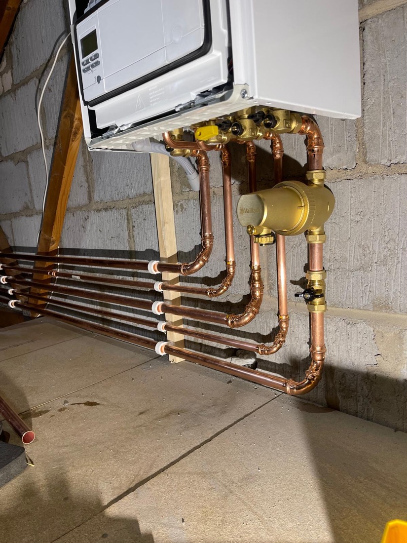A bank of copper pipework with brass isolating valves run to a boiler in a plant room